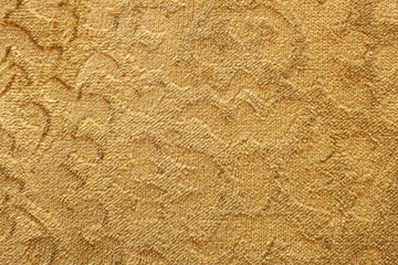 A golden velvet upholstery with an intricate jacquard pattern. The soft and slightly fuzzy texture of the fabric, along with the woven floral design, brings a sense of sophistication and comfort.
