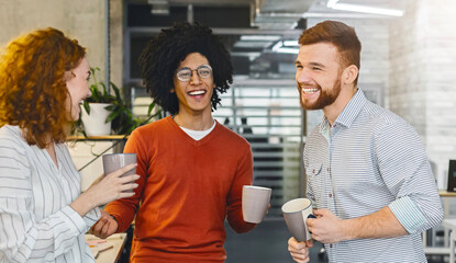 Enjoying free time. Group of millennial coworkers drinking coffee and talking in modern coworking space