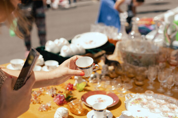 Middle-aged woman taking a photo of a vintage porcelain dishes on a smartphone on flea market. Garage sale, reuse the clothes, second hand and eco consumer. Close-up. Selective focus.