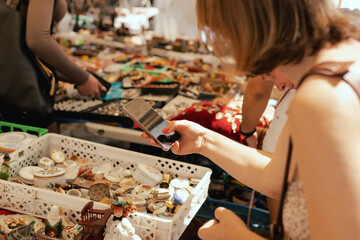 Middle-aged woman taking a photo of a vintage porcelain dishes on a smartphone on flea market....