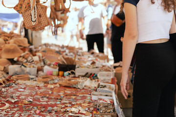 Female shopper picks out a handcrafted jewelry from a collection on a market stall. Small business and travel shopping experiences concept. Close-up. Selective focus