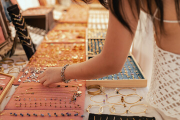 Female shopper picks out a handcrafted jewelry from a collection on a market stall. Small business and travel shopping experiences concept. Close-up. Selective focus