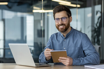 Portrait of a young smiling man in glasses working and studying in the office, sitting at a table...