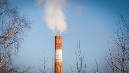 A tall brick chimney with white stripes is spewing smoke into the sky. The sky is clear and blue, and the chimney is the only thing visible in the image.