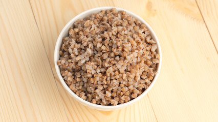 buckwheat porridge in a round white plate on a wooden table. Close-up view from above