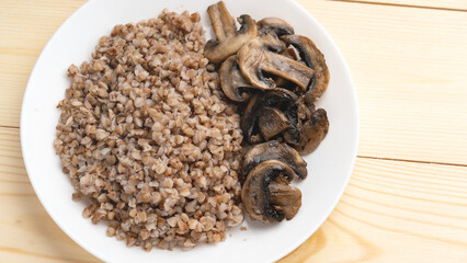 Buckwheat porridge with fried mushrooms on a plate on a wooden background. Closeup. Healthy diet food. The concept of healthy eating