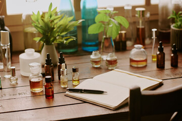 Medium close up of wooden table with small bottles with perfume and perfumers notebook