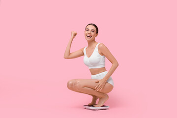 Diet and weight loss concept. Happy young woman on floor scale against pink background