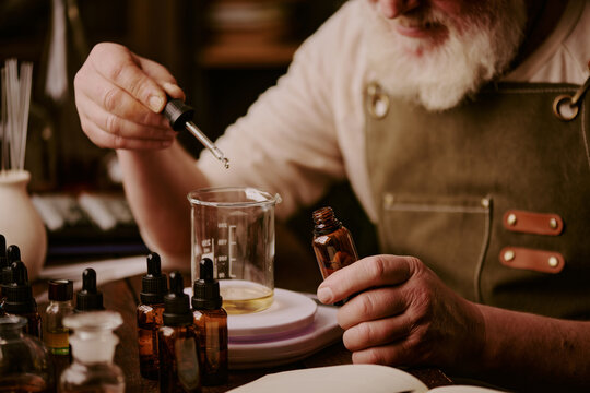 Senior perfumer using glass pipette and crystal flask while mixing different essential oils