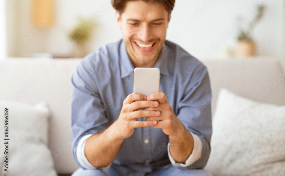 Poster happy man texting at phone. guy playing on smartphone sitting on sofa at home