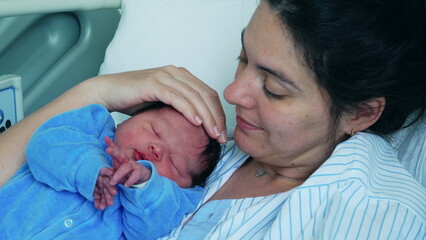 New 30s mother kissing newborn baby on forehead bonding with infant right after childbirth resting...