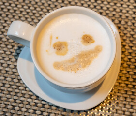 Smiling emoticon on foam coffee in white cup on table in sunlight top view close-up