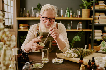 Senior perfumer sitting at his workplace and making new aromatic floral essence for his new female...
