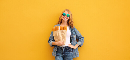 Happy cheerful smiling young woman holding grocery shopping paper bag with white bread baguette