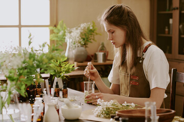 Female young intern mixing dried crushed daisy petals with organic light green liquid