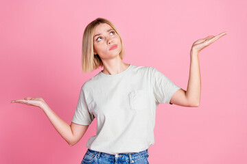 Photo of minded woman with bob hairdo dressed gray t-shirt arms comparing objects look empty space isolated on pink color background