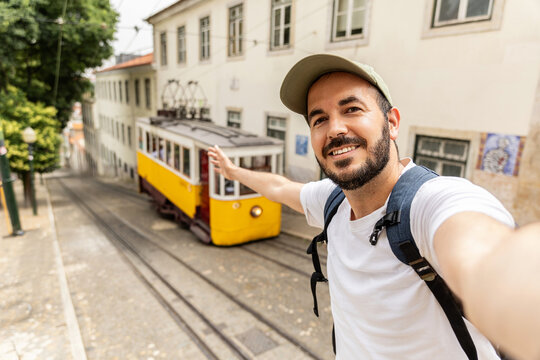 Happy traveler man enjoying summer vacation in Portugal. Smiling tourist taking selfie with yellow Lisbon tran during Europe holidays.