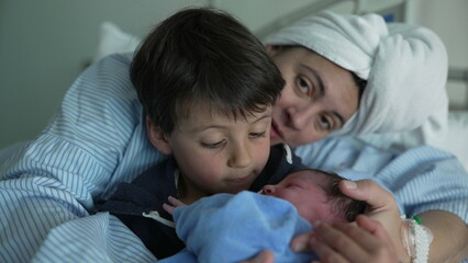 Tender Hospital Introduction of Newborn to Family - Young brother holds new baby while mother watches the siblings connect for the first time