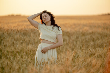 A young brunette walks in wheat fields at sunset in summer. Growing organic wheat and barley.