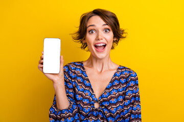 Naklejka premium Portrait of impressed reaction young woman wearing vintage blouse holding smartphone display amazed isolated on yellow color background