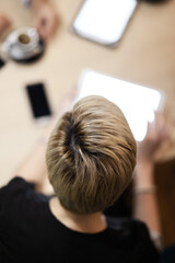 An engaging photo capturing an overhead view of a blonde woman using a tablet during a professional business meeting, with colleagues and devices in the background.