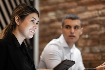 A young woman with a bright smile engages in a discussion with a male colleague in a contemporary brick office setting.
