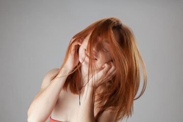 An emotional portrait of a young redhead woman with her flowing hair covering her face, set against a neutral grey backdrop.