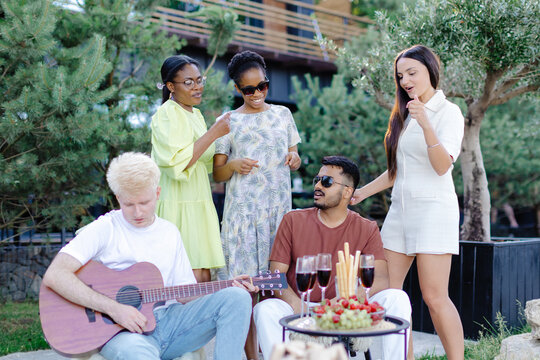 Multicultural group of people, man playing guitar and friends dancing, singing and having fun - Powered by Adobe