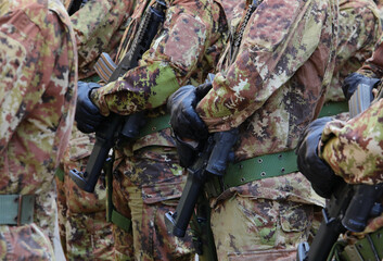 squad of soldiers in green and brown camouflage uniforms, black gloves, and assault rifles in their hands.