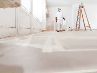 Mold removal service professional worker wearing a protective suit, and respirator mask using products for mold remediation and repainting walls at home renovation site. Concept of home refurbishment