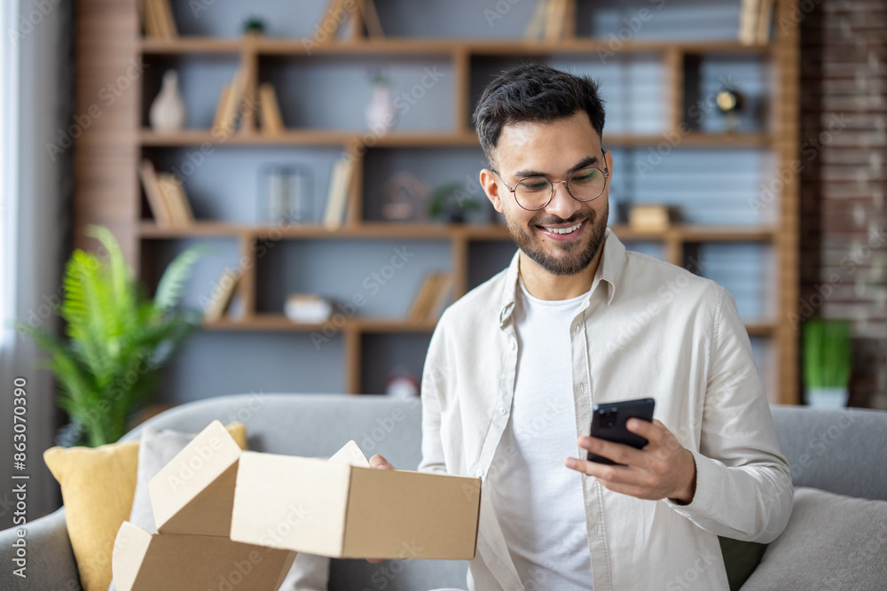 Wall mural close-up photo of an indian smiling young man who received a parcel, holds a box in his hands and di