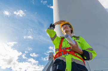 woman in a safety vest is on a ladder next to a wind turbine