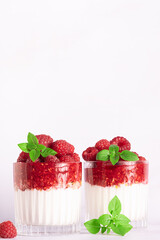 Tasty homemade yogurt parfait with granola, raspberry sauce, fresh raspberries and aromatic basil leaves in a glass on light marble background close up, healthy low carb dessert concept.