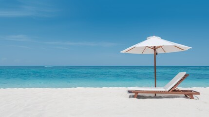 Comfortable chaise lounge with a sun umbrella on a beautiful sandy beach, calm blue sea and sunny skies creating the ideal beach retreat