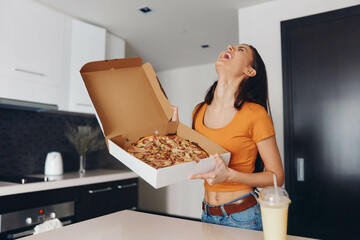 Woman holding a box of pizza in kitchen setting, standing in front of counter, ready to enjoy a meal