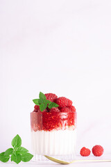 Tasty homemade yogurt parfait with granola, raspberry sauce, fresh raspberries and aromatic basil leaves in a glass on light marble background close up, healthy low carb dessert concept.