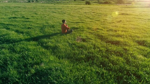 UHD 4K aerial view. Low altitude radial flight over sport yoga man at perfect green grass. Sunset in mountain. Green meadow and sun rays on horizon. Fast orbital movement.