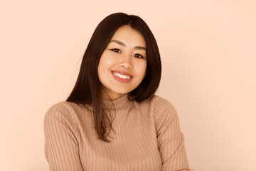 A young woman with long black hair smiles brightly against a beige backdrop.