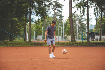Soccer player in 20s plays with a balloon on a clay court. Amateur sport. Individual football training. Soccer. Kicking, striking, passing and dribbling