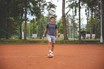 Soccer player in 20s plays with a balloon on a clay court. Amateur sport. Individual football training. Soccer. Kicking, striking, passing and dribbling