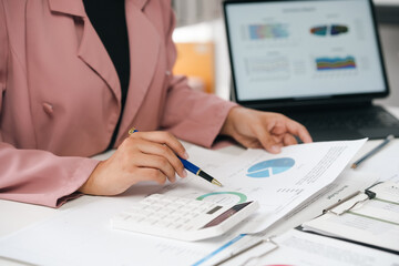 Businesswoman analyzing financial charts and using calculator in office