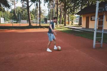 Black-haired athlete plays with a balloon on a clay court. Amateur sport. Individual football training. Soccer. Kicking, striking, passing and dribbling
