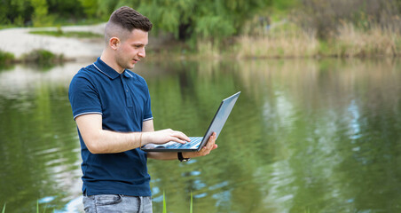 Young man works on a laptop while outdoors. He is a freelance ecologist studying the environment. Working outdoors is the best alternative to the office. Water analysis.