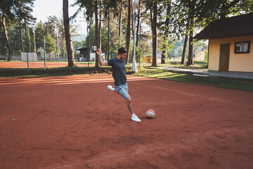 Black-haired athlete plays with a balloon on a clay court. Amateur sport. Individual football training. Soccer. Kicking, striking, passing and dribbling