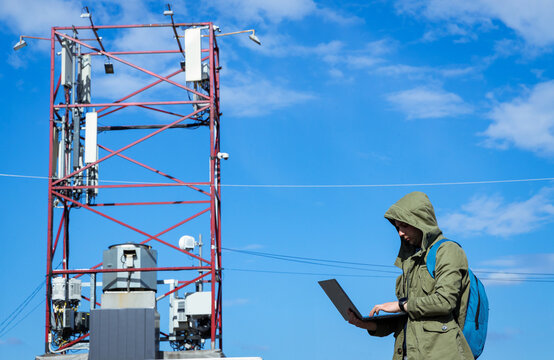 Technician programmer connects remotely to transfer data. Male telecommunications engineer works near a communication tower to check maintain 4G and 5G internet networks and cellular communications.