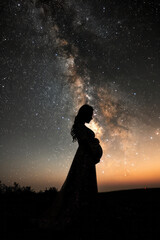 Fototapeta premium Silhouette of a pregnant woman outlined by a galaxy of stars, merging with the cosmos,