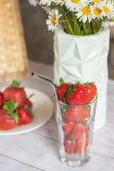 Red strawberries on kitchen table in glass and plate, summer still life, vase of daisies. High quality photo