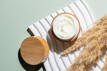 Top view of collagen cream in open bamboo jar and dry flowers reeds on greene background. Set for skin and body care beauty products