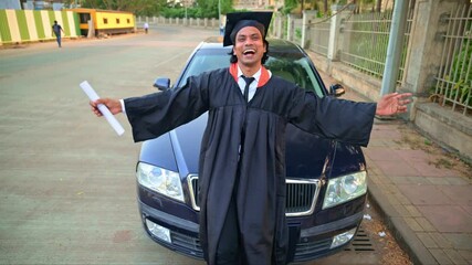 Joyful graduate outstretch hands front of a car