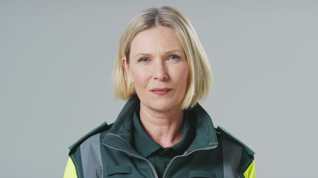 Serious mature female paramedic wearing uniform in front of plain studio background - shot in slow motion
